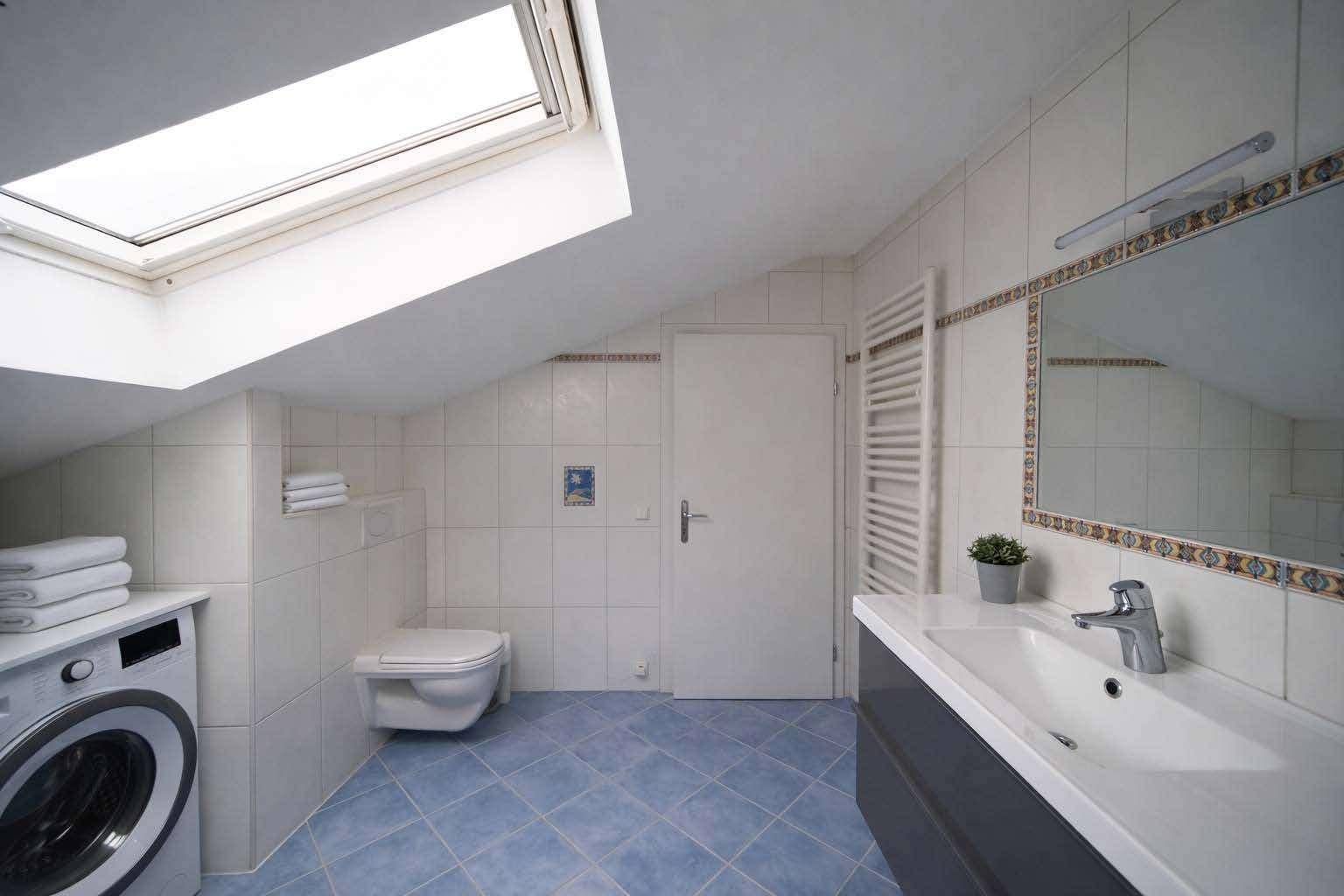 Helles Badezimmer mit Dachfenster, WC, Waschmaschine und blauen Fliesen.