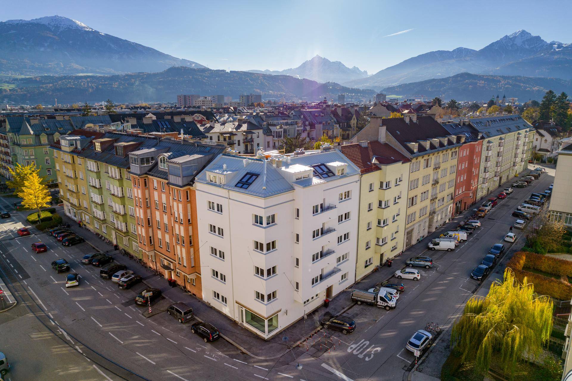 Luftaufnahme eines modernen Eckgebäudes in einer Stadt mit beeindruckendem Bergpanorama im Hintergrund.