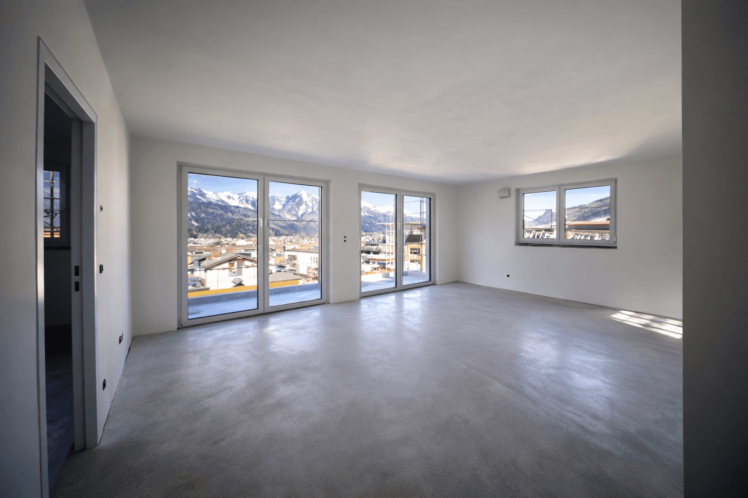Fertiggestellter, leerer Wohnraum mit poliertem Betonboden und Panoramablick auf Berge und Stadt.