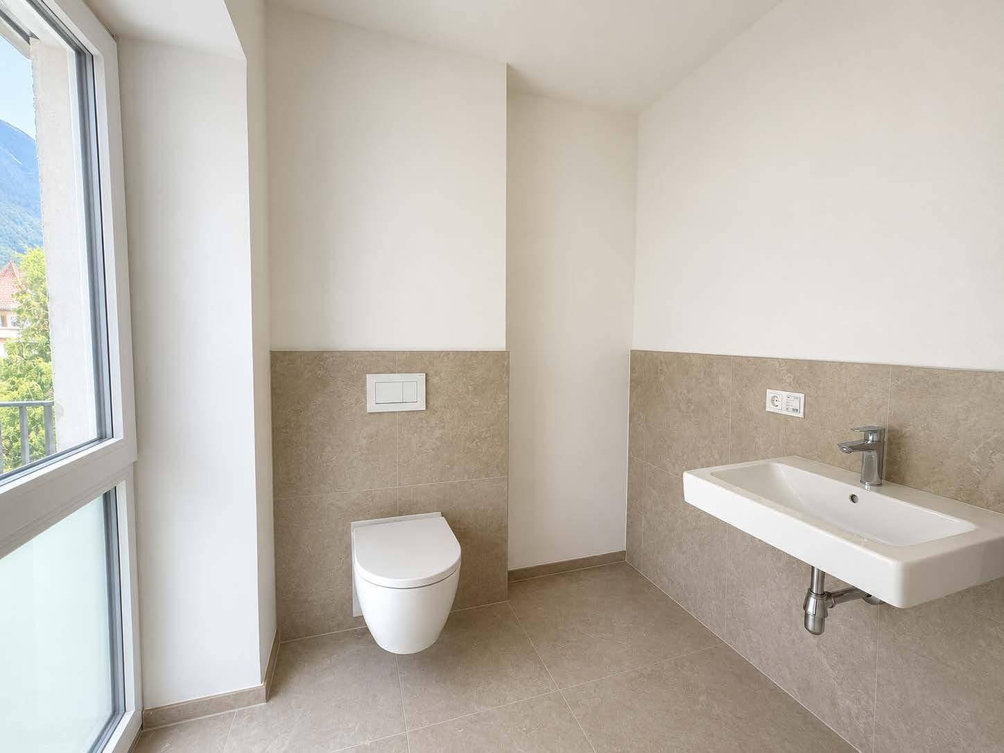 Modernes Gäste-WC mit Wand-WC, Waschbecken und Fenster mit Bergblick.