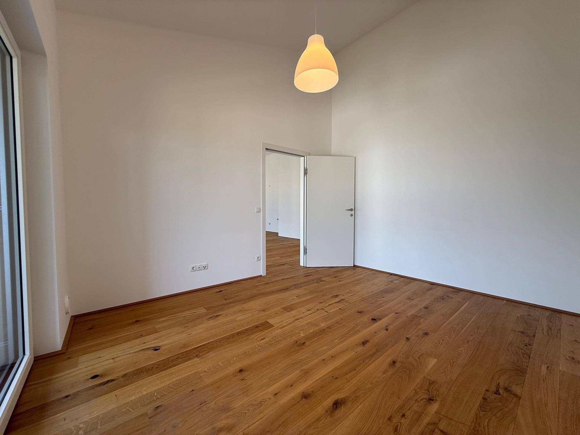 Leeres Zimmer mit Holzboden und Zugang zu einem weiteren Raum, ideal als Schlaf- oder Arbeitszimmer.