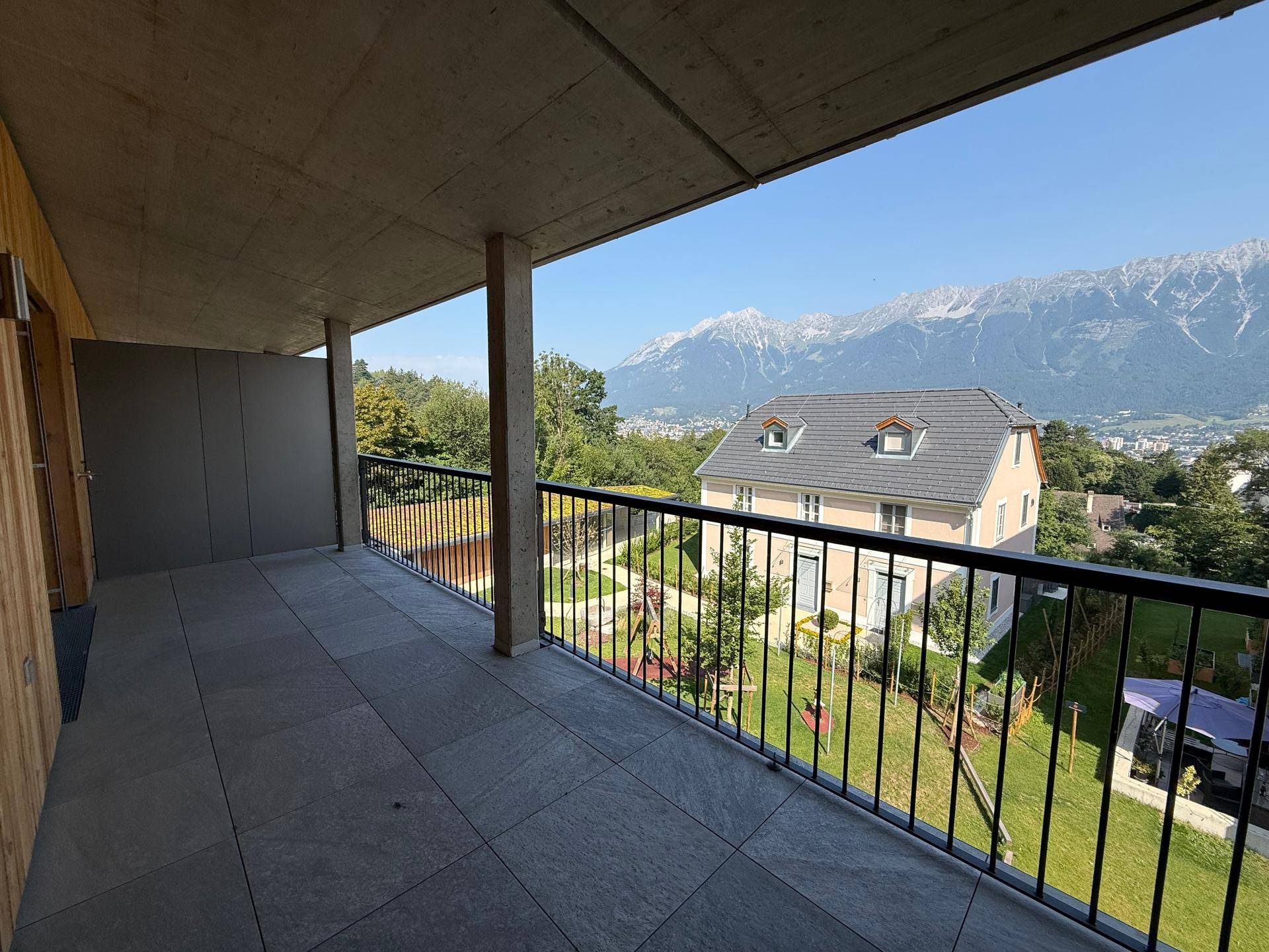 Geräumiger Balkon mit Fliesen und Bergblick, umgeben von viel Grün.