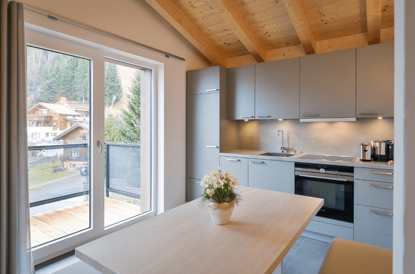 Moderne Küche mit Essbereich, grauen Schränken und Balkonzugang mit Bergblick.