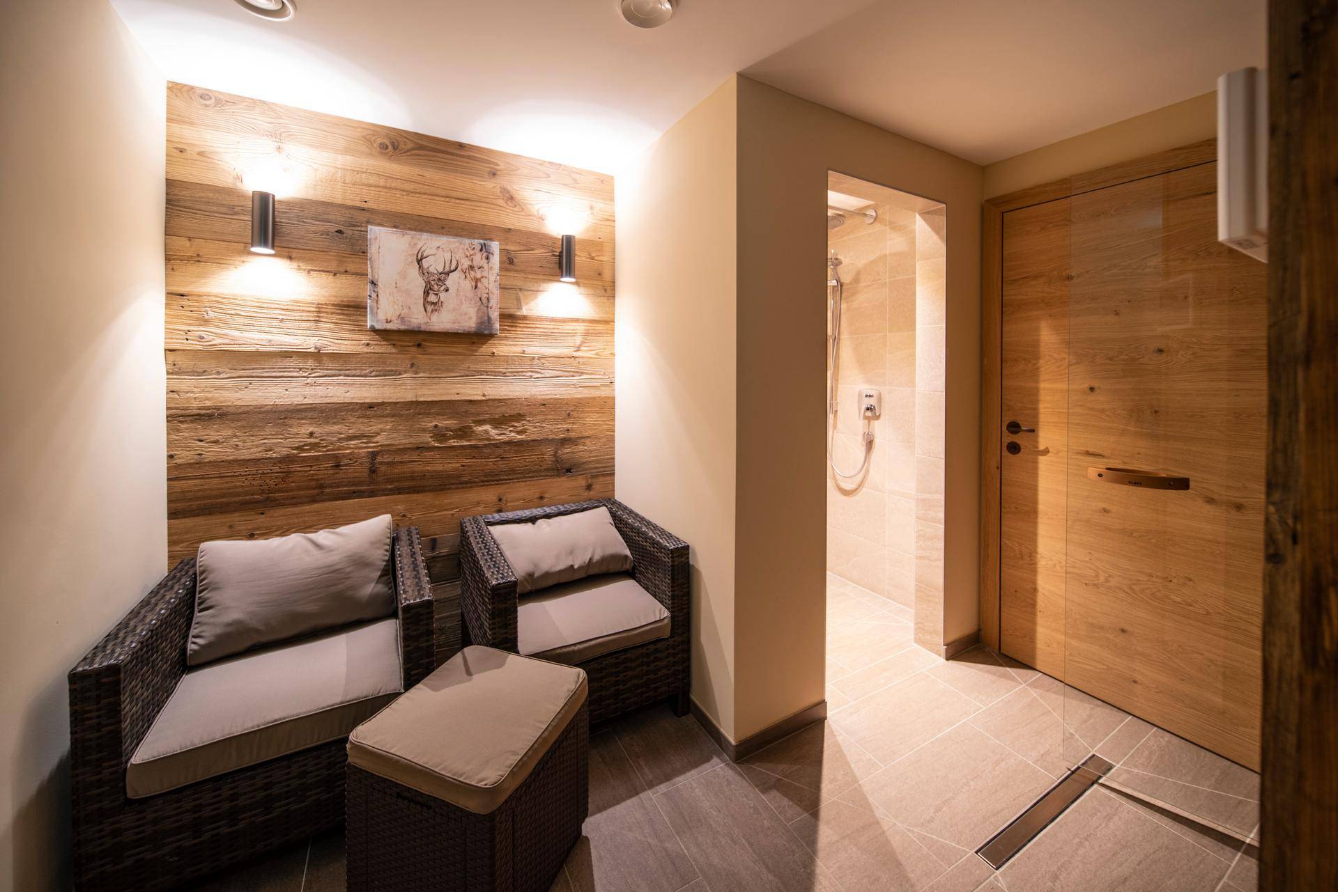 Entspannungsbereich mit Holzwand, bequemen Sesseln und Zugang zur Dusche.