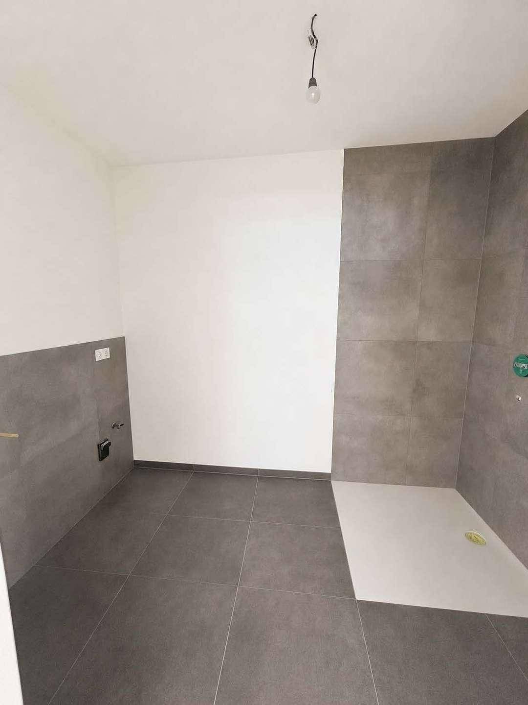 Modernes Badezimmer mit grauen Fliesen und vorbereiteter Duschfläche, unmöbliert.