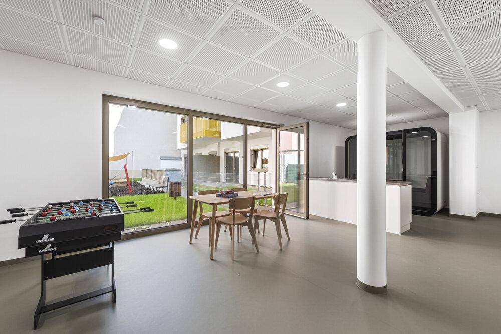 Gemeinschaftsraum mit Tischfußball, Esstisch und großen Fenstern zum Außenbereich.