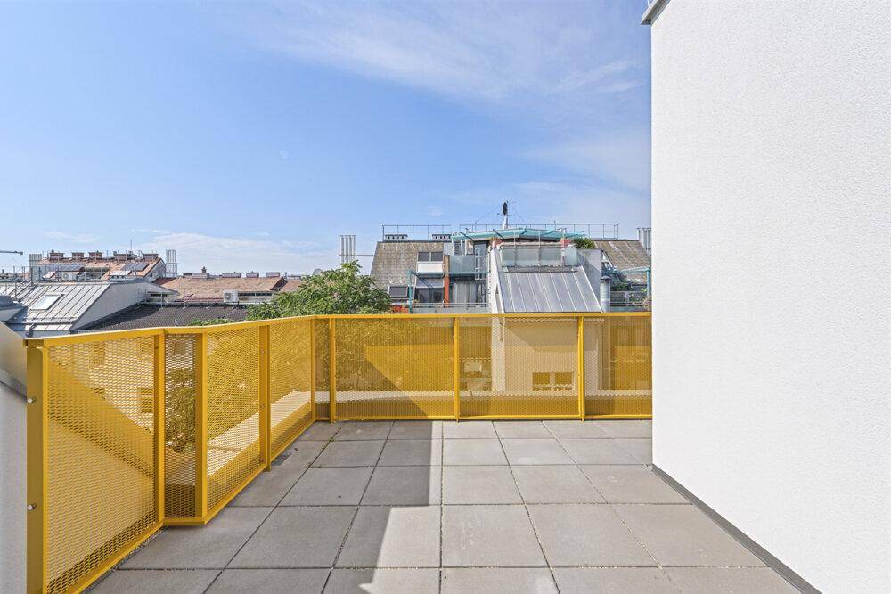 Sonniger Terrassenbereich mit gelbem Metallgeländer und Blick auf die umliegenden Dächer.