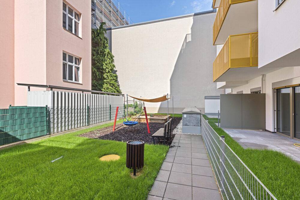 Gepflegter Gemeinschaftsgarten mit Spielbereich, Rasen und schattenspendendem Sonnensegel.