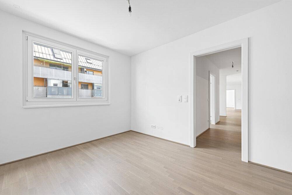 Leeres Zimmer mit Parkettboden und weiß gestrichenen Wänden, mit Zugang zum Flur.