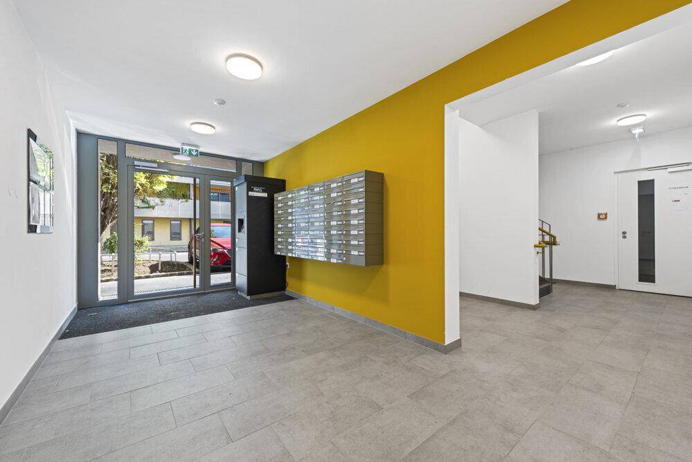 Heller Eingangsbereich eines modernen Wohngebäudes mit Briefkästen und gelber Wand.