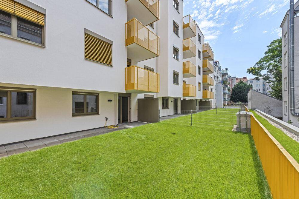 Moderne Wohnanlage mit weißer Fassade, gelben Balkonen und gepflegter Rasenfläche.