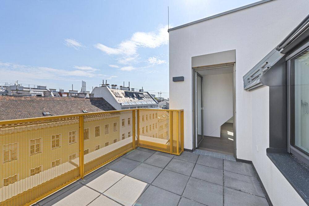 Sonnige Dachterrasse mit gelbem Gittergeländer und weitem Blick über die Dächer der Stadt.