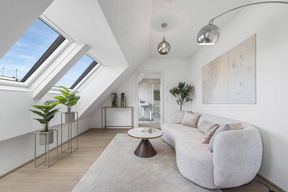Helles Wohnzimmer mit modernen Möbeln, großen Dachfenstern und Blick in ein angrenzendes Bad.