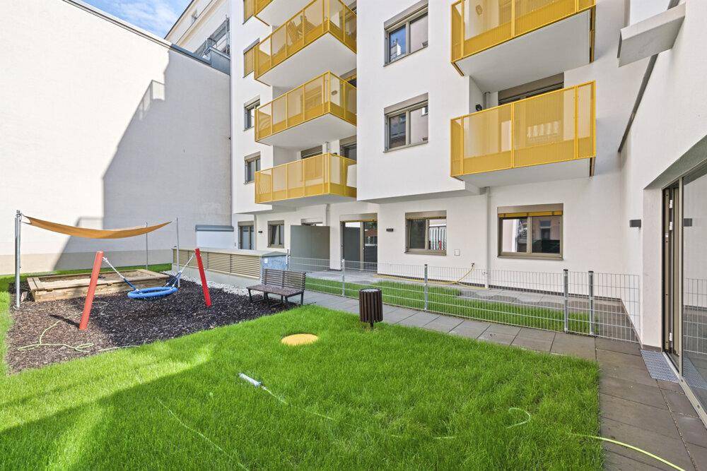 Grüner Gartenbereich mit Kinderspielplatz, Schaukeln und Sandkasten neben dem Gebäude.