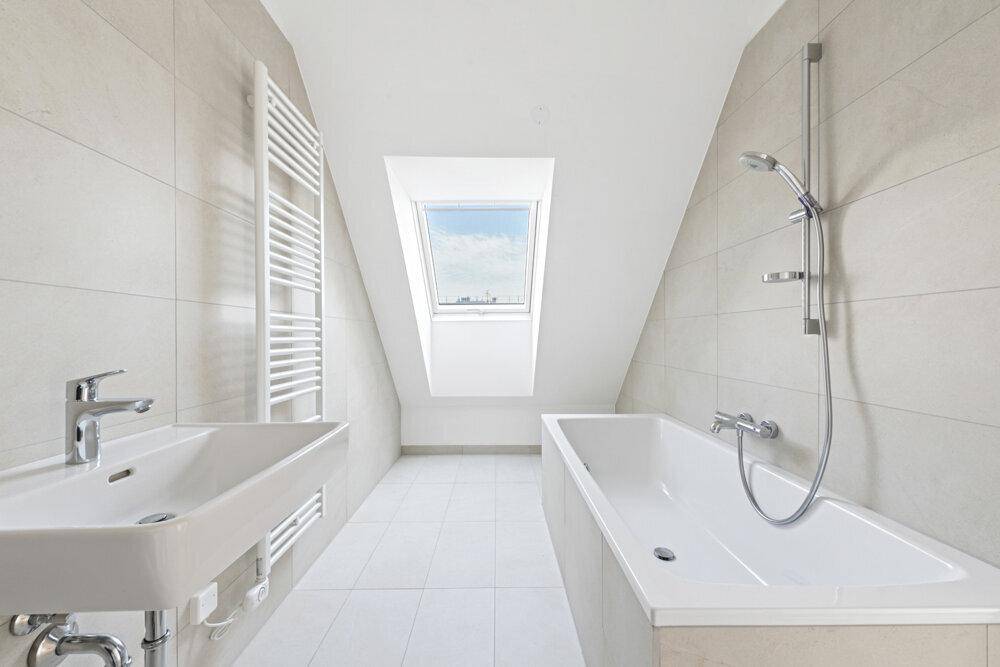 Modernes Badezimmer im Dachgeschoss mit Badewanne, Waschbecken und Dachfenster für natürliches Licht.