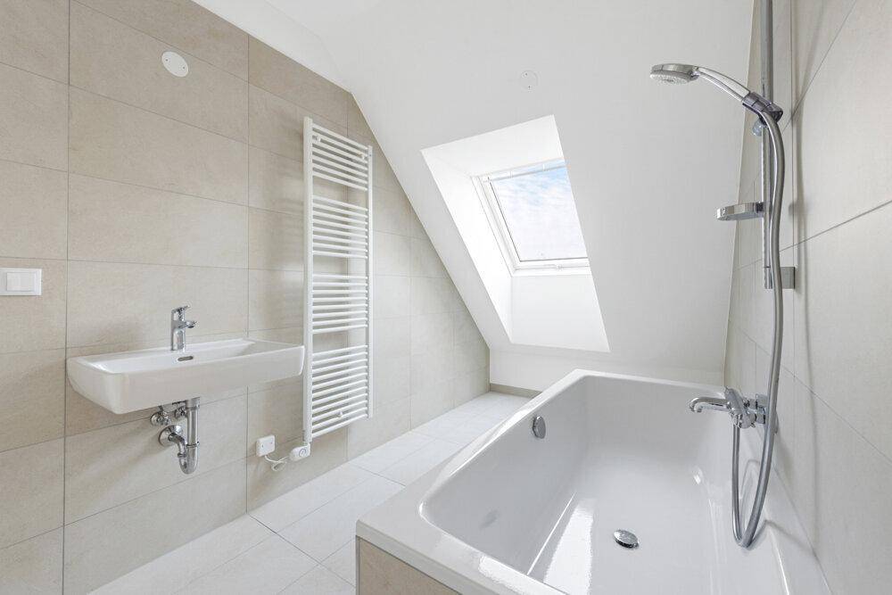 Modernes Badezimmer im Dachgeschoss mit Badewanne, Waschbecken und Dachfenster.