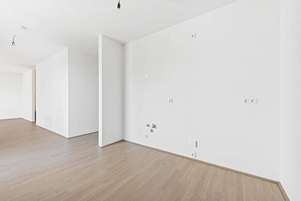 Leerer Küchenbereich mit Anschlüssen für eine Einbauküche und hellem Parkettboden.