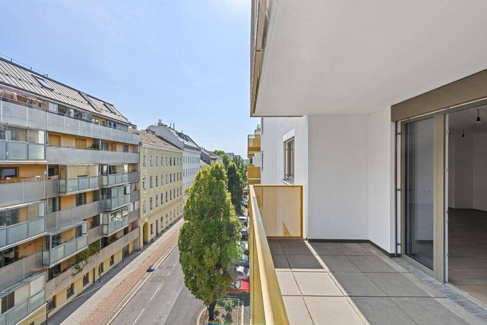 Langer Balkon mit Fliesenboden und Blick auf die Stadtstraße mit Bäumen.