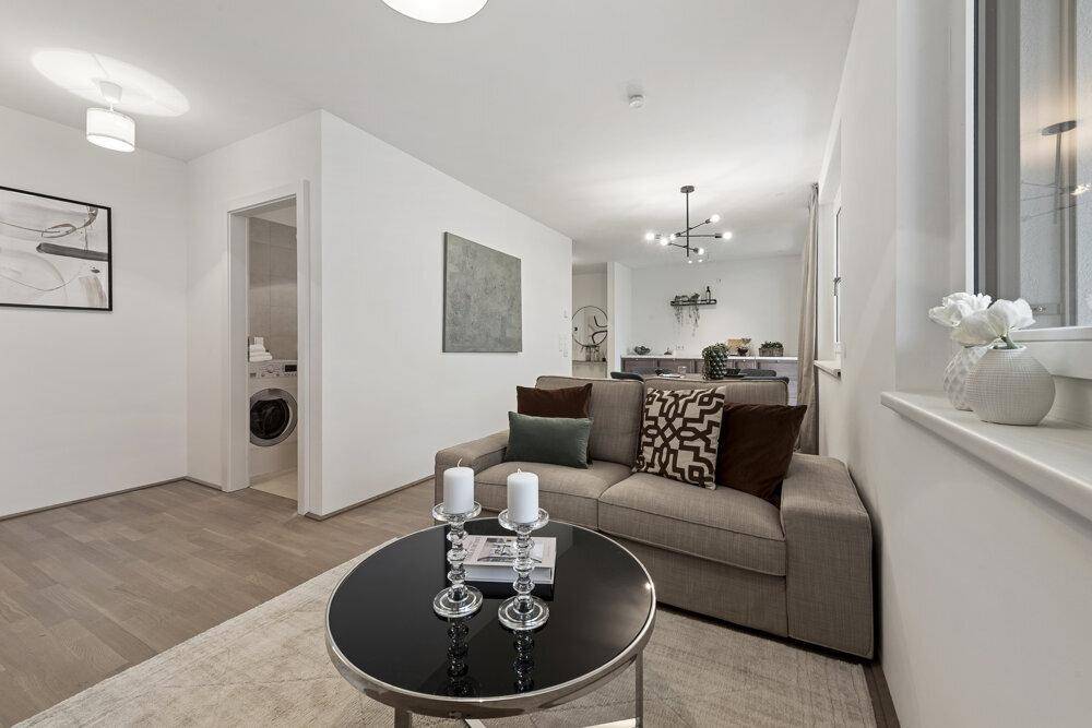 Gemütlicher Wohnbereich mit beigem Sofa, Couchtisch und Blick auf den Essbereich und ein Badezimmer.