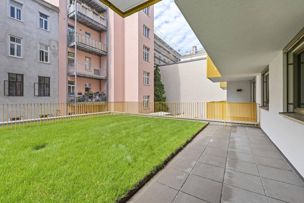 Geräumige Terrasse mit Betonplatten und angrenzender Rasenfläche im Innenhof.