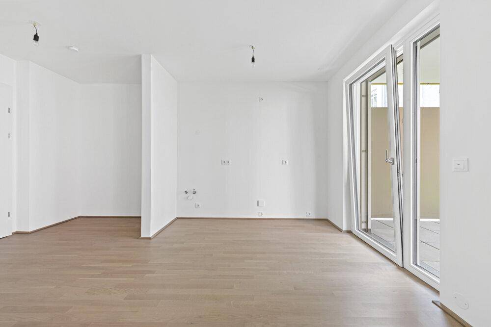 Geräumiger, unmöblierter Wohnbereich mit großen Fenstern und hellem Parkettboden.