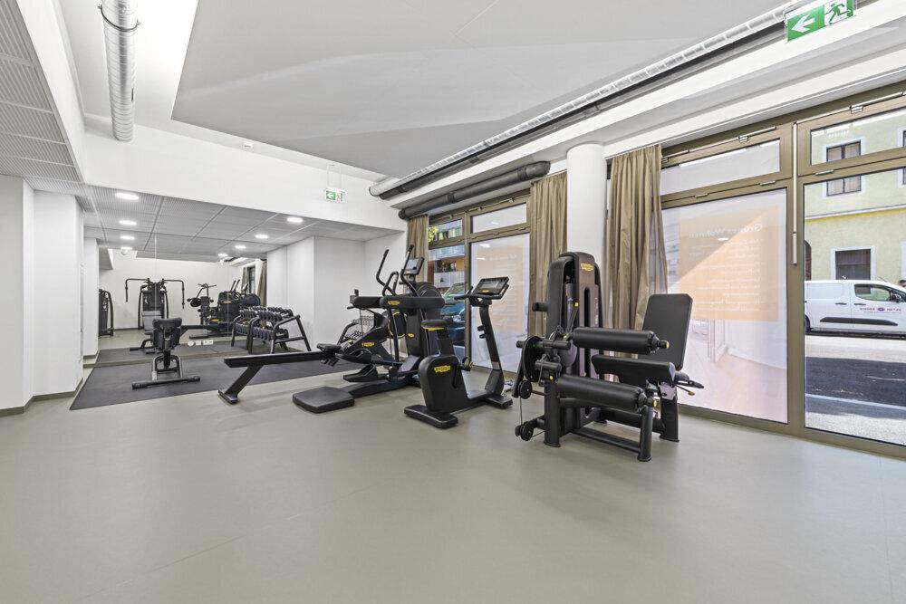 Gut ausgestatteter Fitnessraum mit verschiedenen Trainingsgeräten und großen Fenstern.