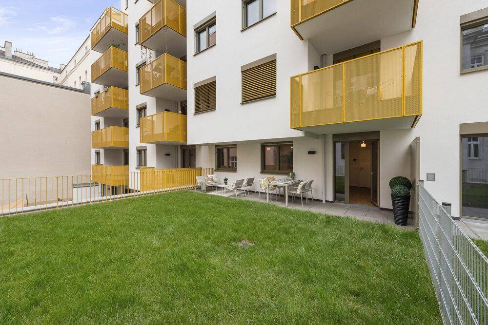 Außenansicht eines modernen Gebäudes mit gepflegtem Rasen und möblierter Terrasse.