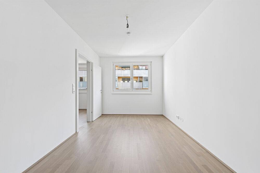 Leeres Zimmer mit Parkettboden und weiß gestrichenen Wänden, bereit zum Einrichten.