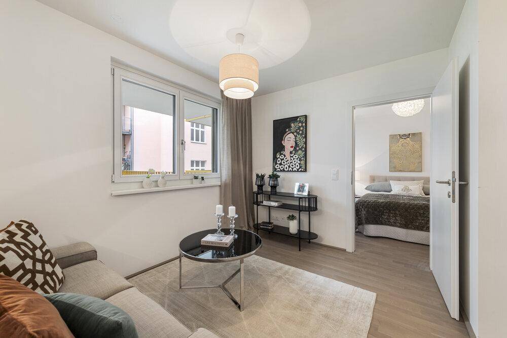 Heller Wohnraum mit Sofa, Couchtisch und direktem Zugang zu einem angrenzenden Schlafzimmer.