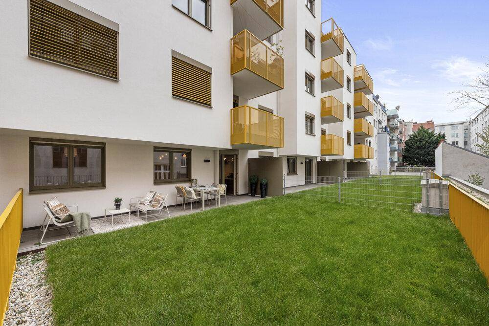 Moderne Wohnanlage mit gepflegtem Rasenbereich und möblierter Terrasse im Erdgeschoss.