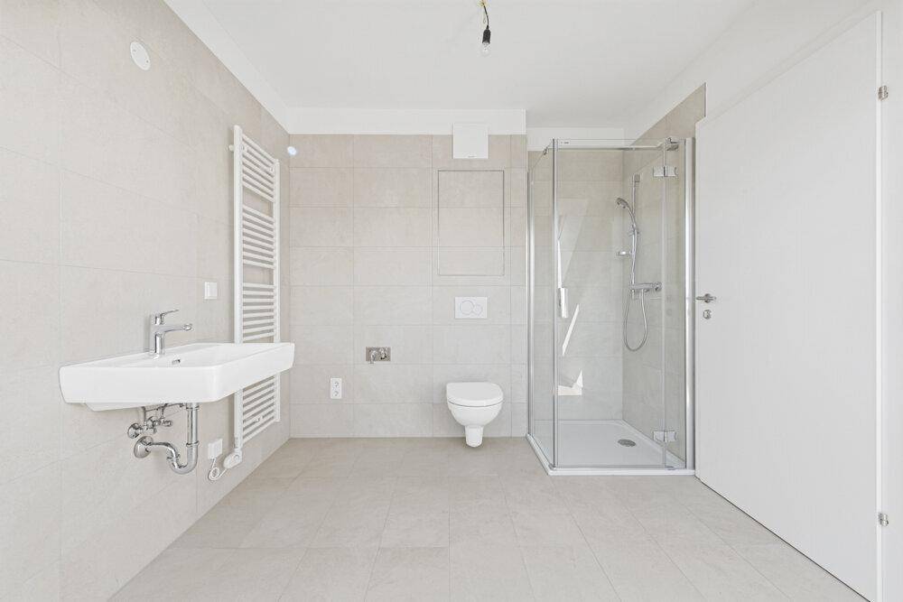 Modernes Badezimmer mit hellgrauen Fliesen, ebenerdiger Dusche und wandhängendem WC.