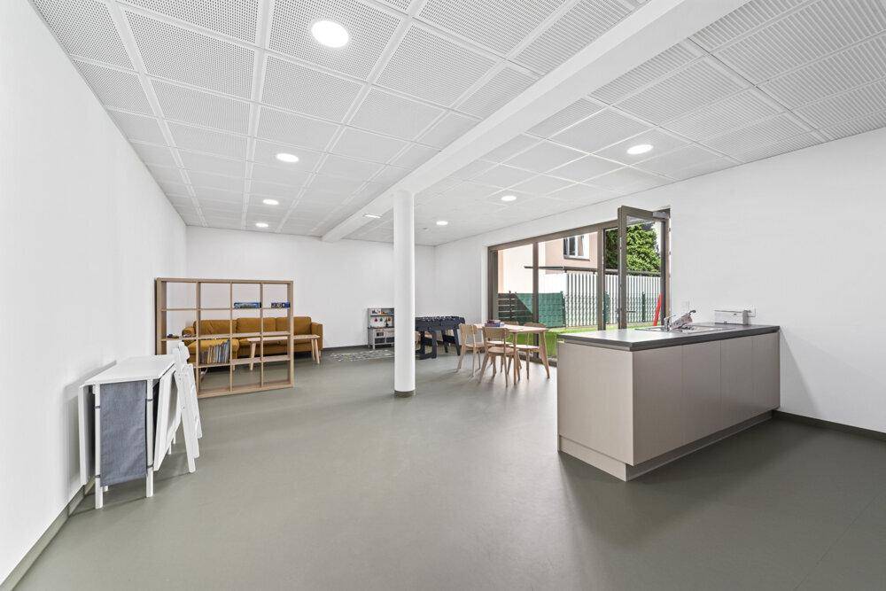 Großer Gemeinschaftsraum mit Küchenzeile, Sitzgelegenheiten und Zugang zum Garten.