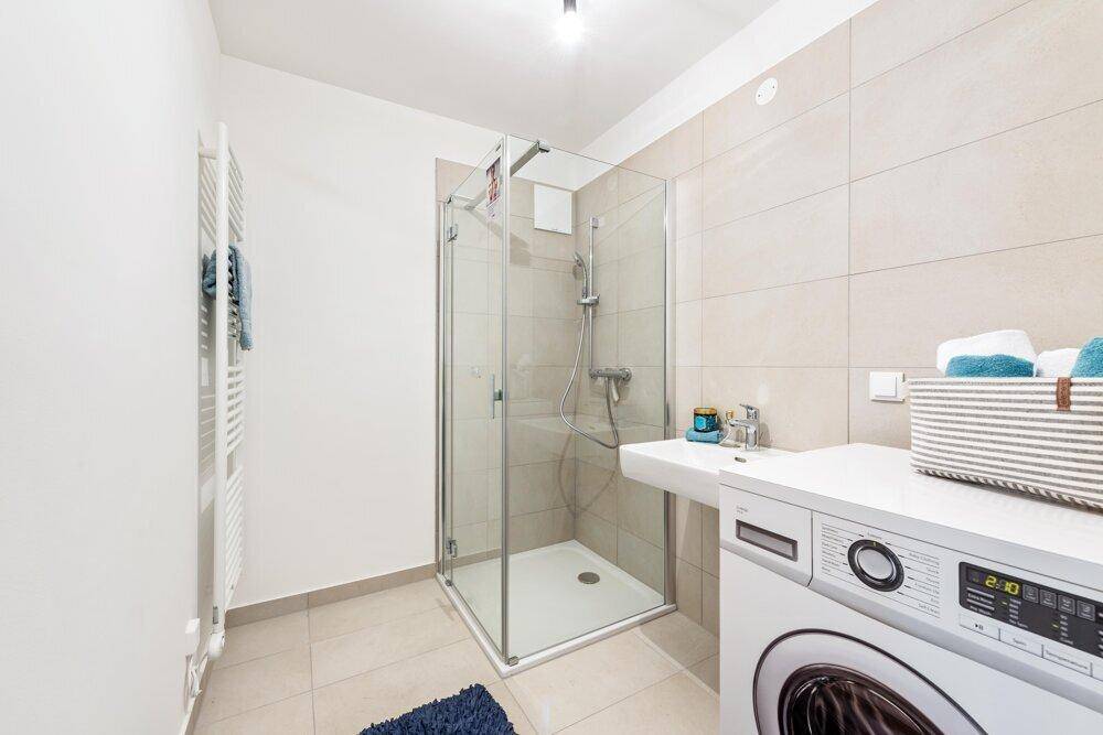 Modernes Badezimmer mit Duschkabine, Waschmaschine und beheiztem Handtuchhalter.