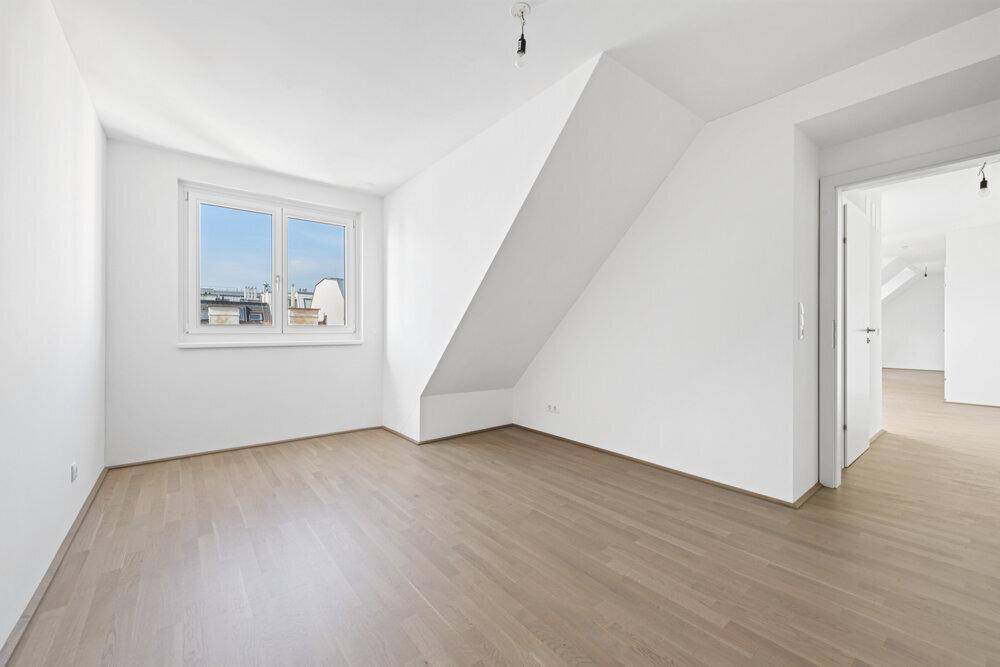 Leeres Zimmer mit Holzboden, Fenster und Schrägdach im Dachgeschoss.