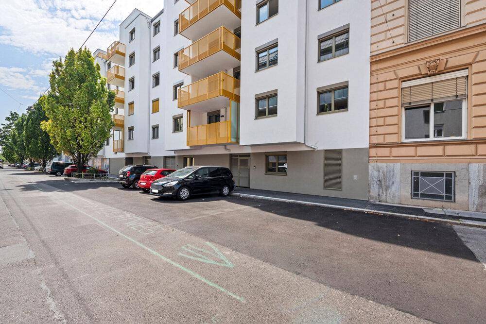 Moderne Wohngebäude-Fassade mit Balkonen und parkenden Autos an der Straße.
