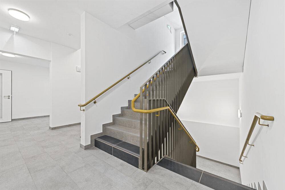 Modernes Treppenhaus mit Metallgeländer und Fliesenboden, das zu den oberen Etagen führt.