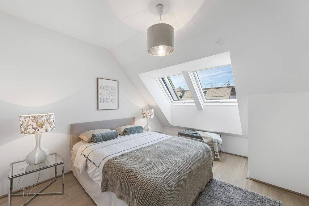 Helles Schlafzimmer mit Dachschrägen, Dachfenstern und Doppelbett.