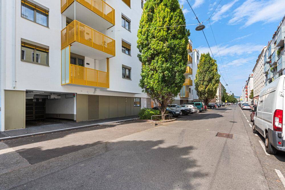 Ansicht der modernen Wohnanlage von der Straße mit Bäumen und parkenden Fahrzeugen.