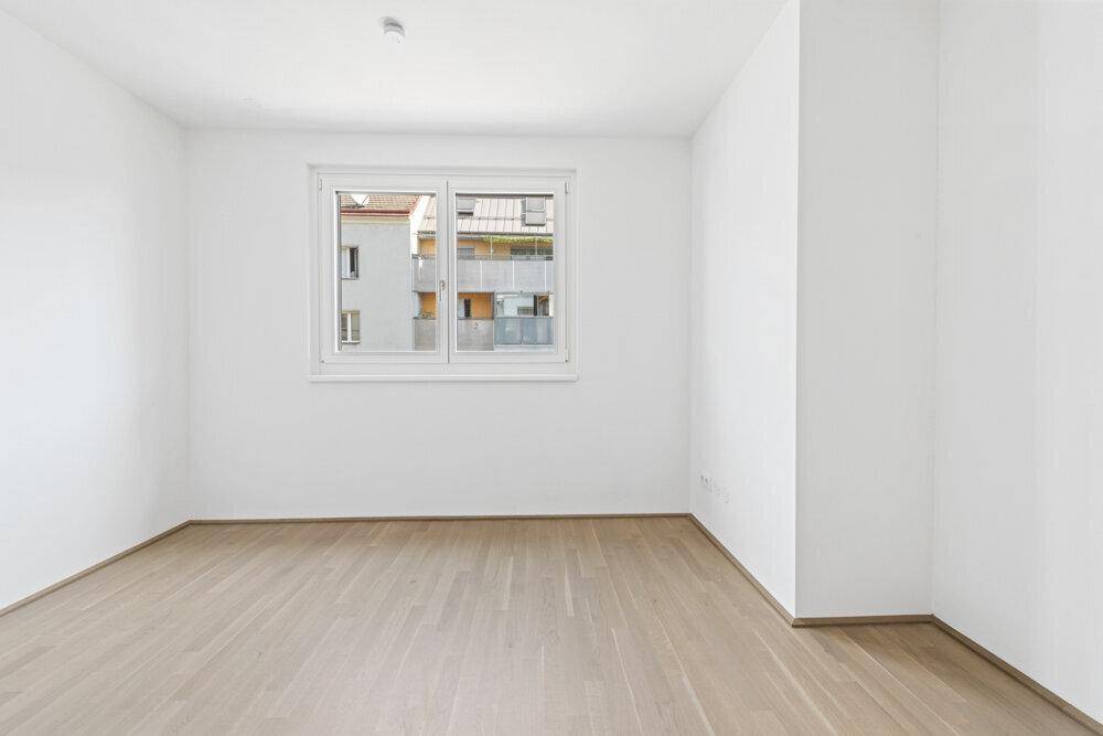 Helles, leeres Zimmer mit Parkettboden und einem großen Fenster für viel Tageslicht.
