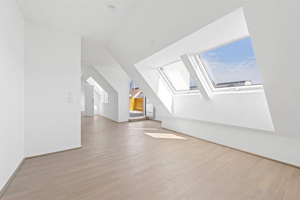 Lichtdurchfluteter Wohnraum mit Dachschrägen, hellen Holzböden und großen Dachfenstern.