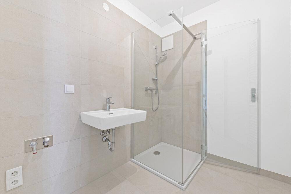 Modernes Badezimmer mit ebenerdiger Dusche und Waschbecken, hell gefliest.