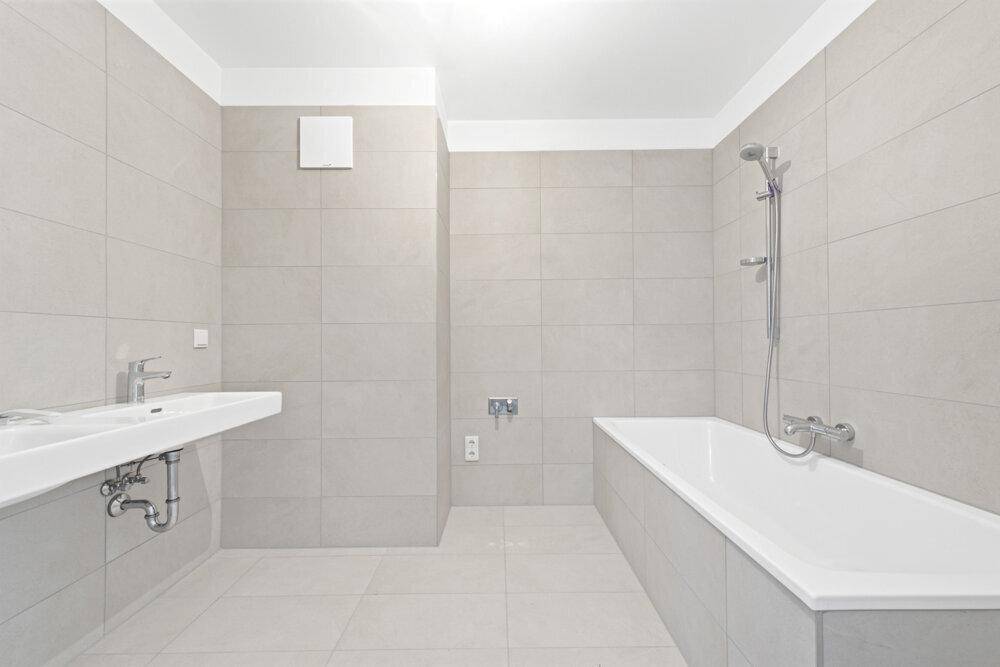 Modernes Badezimmer mit hellgrauen Fliesen, Badewanne und einem einzelnen Waschbecken.