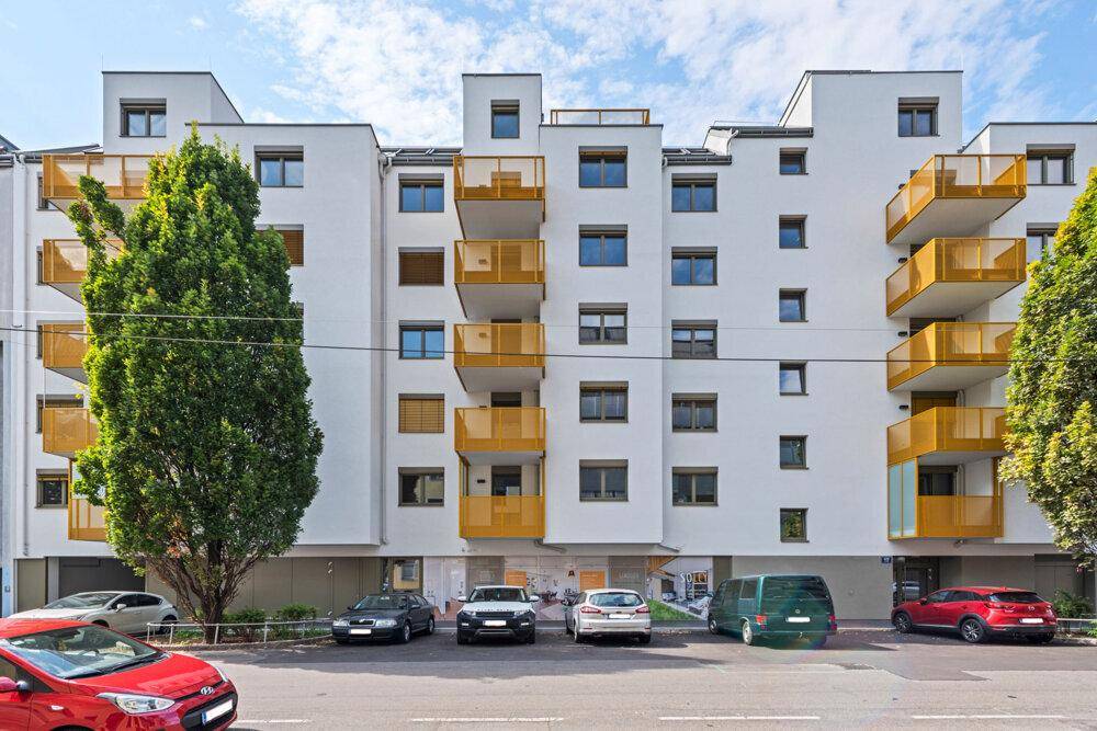 Moderne Wohnhausfassade mit gelben Balkonen und parkenden Autos davor.