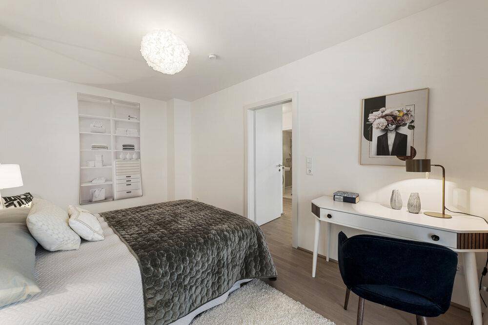 Helles Schlafzimmer mit modernem Bett, Schreibtisch und integrierten Wandregalen für Stauraum.