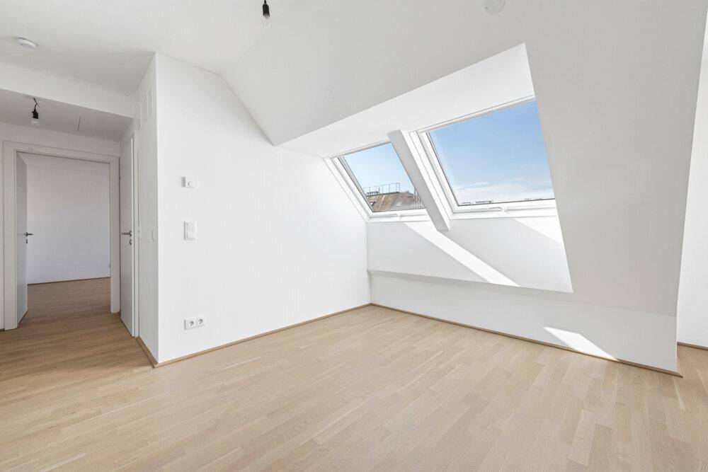 Heller Raum mit Holzboden und Dachfenstern, ideal für ein Schlafzimmer oder Büro.