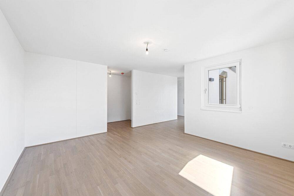 Leerer, heller Raum mit Parkettboden und einem Fenster, ideal für ein Wohnzimmer oder Schlafzimmer.