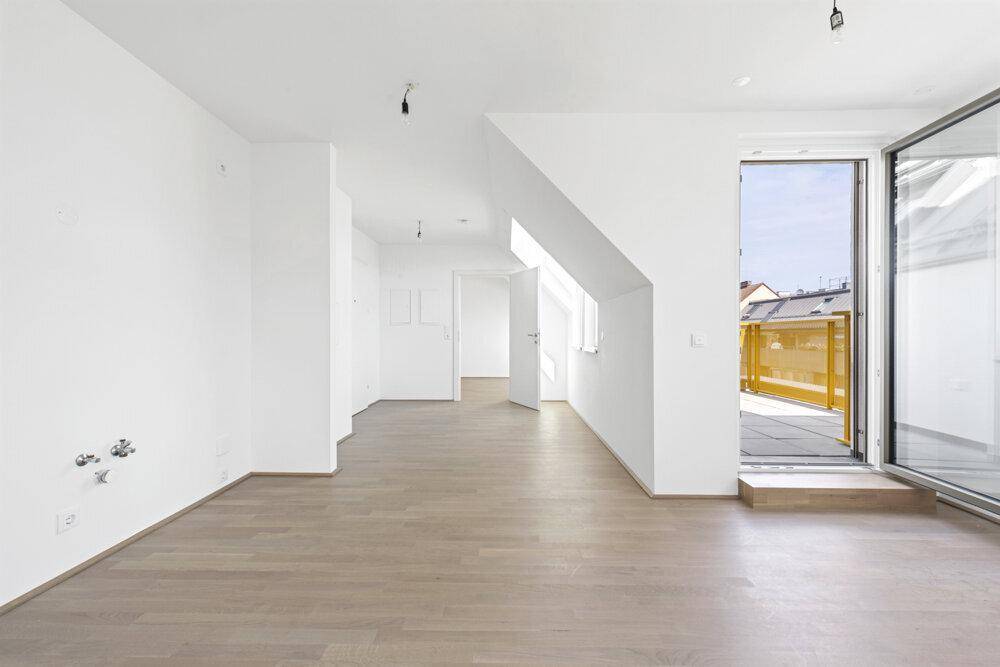 Heller, leerer Wohnraum mit hellem Holzboden, weißen Wänden und Zugang zur Terrasse.