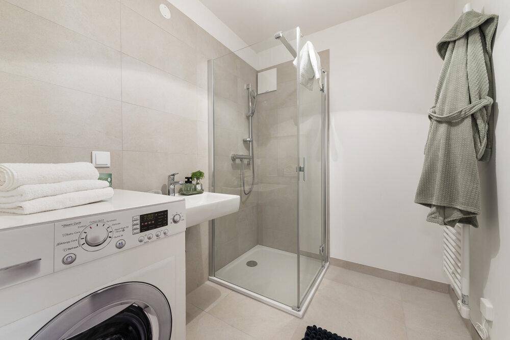 Modernes Badezimmer mit Duschkabine, Waschbecken und integrierter Waschmaschine.