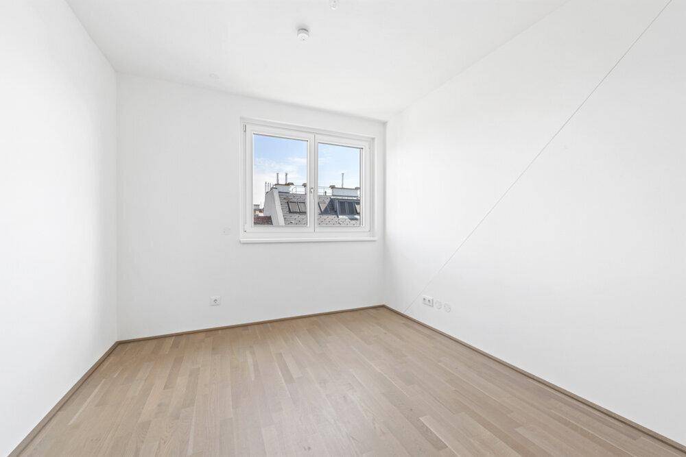 Helles Schlafzimmer mit Parkettboden und Fenster, unter einer Dachschräge gelegen.