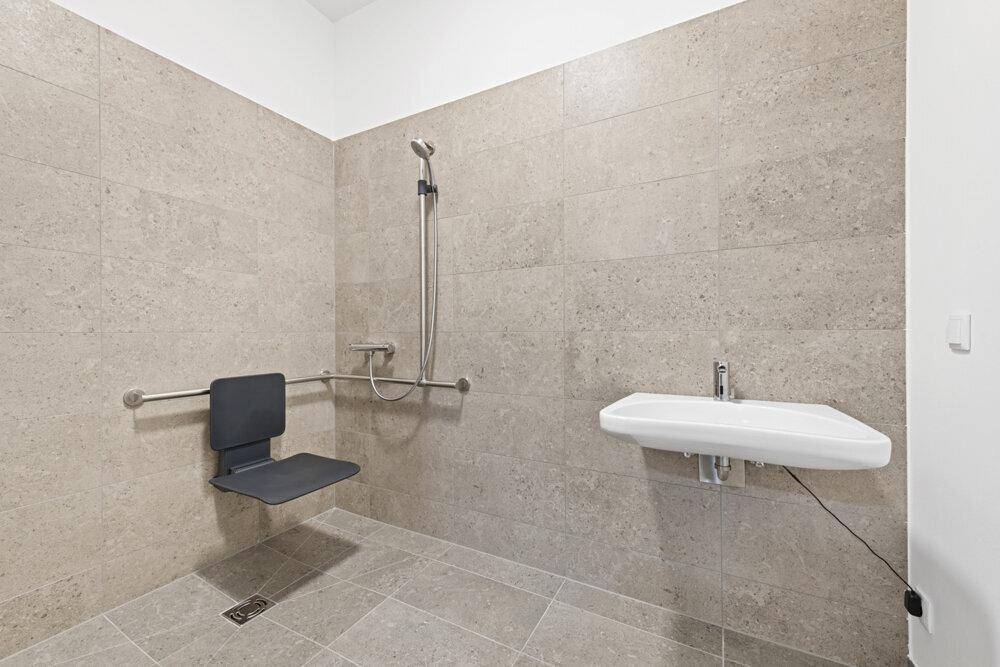 Barrierefreies Badezimmer mit Duschsitz, Haltegriffen und einem wandmontierten Waschbecken.